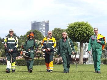 Fünf Menschen laufen über eine Wiese. Sie tragen Arbeitskleidung.