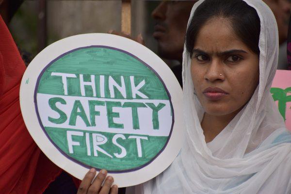 10 Jahre Rana Plaza: Gedenken – Aktiv Werden – Weitersagen 6 Gesundheit und Sicherheit am Arbeitsplatz Eine ernst blickende Frau mit Kopftuch hält ein Schild hoch. Darauf steht "Think Safety First"