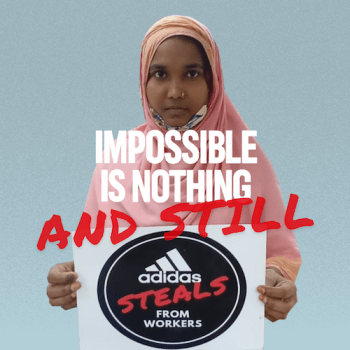 Ein Mädchen mit Kopftuch hält ein Schild hoch. Darauf steht: "adidas steals from workers"