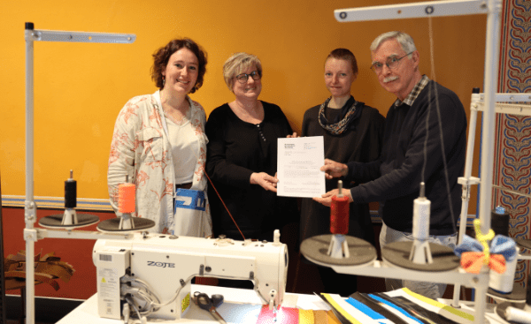 Spenden für die Kampagne für Saubere Kleidung | Clean Clothes Campaign Germany 12 Drei Frauen und ein Mann stehen hinter einem Nähtisch und halten ein Dokument in die Kamera.