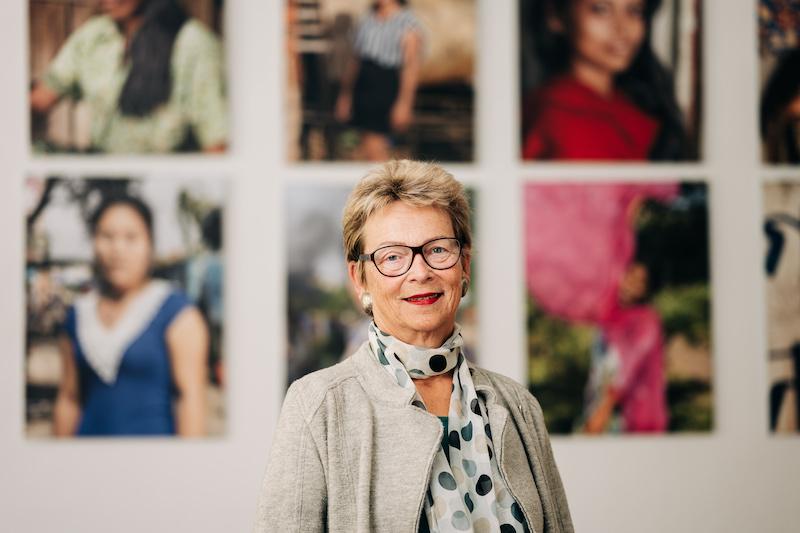 Eine Frau mit kurzen Haaren und Brille steht vor großen Fotografien von Frauen.