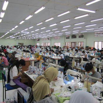 In einer riesigen Fabrikhalle sitzen Arbeiterinnen an ihren Nähmaschinen