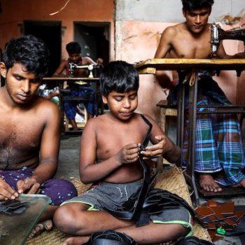Kinderarbeit und Leder 1 Vision Mission Kampagne für Saubere Kleidung Ein Kind und ein junger Mann sitzen auf dem Boden und nähen mit der Hand Leder. Im Hintergrund arbeiten zwei Männer an Nähmaschinen.