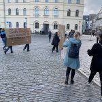 Auf einem kopfsteingepflasterten Platz stehen Menschen mit Plakaten.