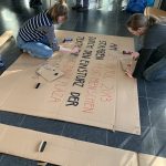 Eine Frau und ein Mann knien am Boden und malen auf einen großen Karton.