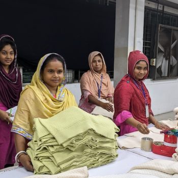 Bangladesch: Speakerstour 11 Jahre nach Rana Plaza 3 Vier bangladeschische Frauen stehen hinter einem Tisch voller Stoffe.