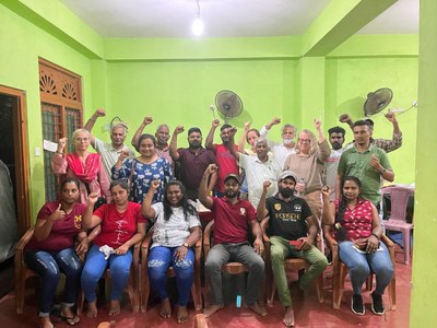 Spenden für die Kampagne für Saubere Kleidung | Clean Clothes Campaign Germany 7 In einem Raum mit grünen Wänden reckt eine Gruppe Menschen ihre Fäuste in die Luft.