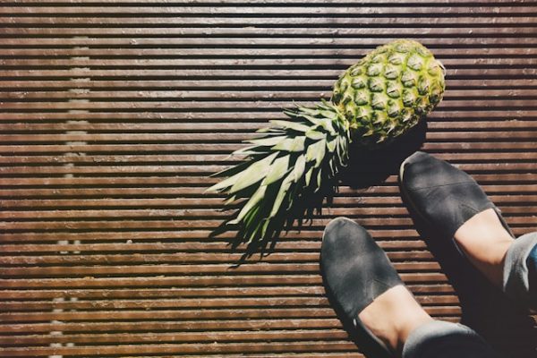 Eine Person, von der nur die Füße zu sehen sind, steht vor einer Ananas