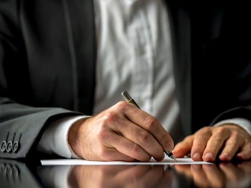 Spenden für die Kampagne für Saubere Kleidung | Clean Clothes Campaign Germany 4 Ein Mann im Anzug schreibt auf ein Papier.