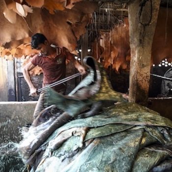 Ein Mann mit nacktem Oberkörper steht hinter gestapelten Leder. Flüssigkeit spritzt.