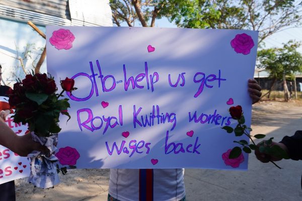 "Wir bitten nur um Gerechtigkeit" - Entlassene Arbeiter*innen gegen OTTO 14 Ein Mensch hält ein Plakat hoch. Andere halten Blumen ins Bild.