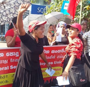 Union Busting: Wer kämpft, wird bedroht 4 Menschen stehen um ein rotes Plakat. Eine Frau im Vordergrund reckt die Faust nach oben.