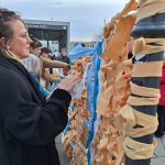 Eine Frau steht vor einer Stele voller Stoffstreifen