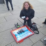 Eine Frau kniet auf der Straße. Sie hat eine Sprühdose in der Hand