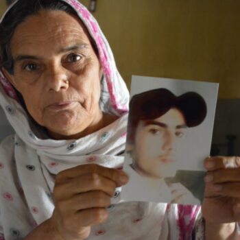 13 Jahre Ali Enterprises: Solidarität mit den Überlebenden und ein Appell an die Marken 6 Eine ältere Frau mit Kopftuch hält ein Foto hoch. Darauf zu sehen ist ein junger Mann mit Baseball-Mütze.