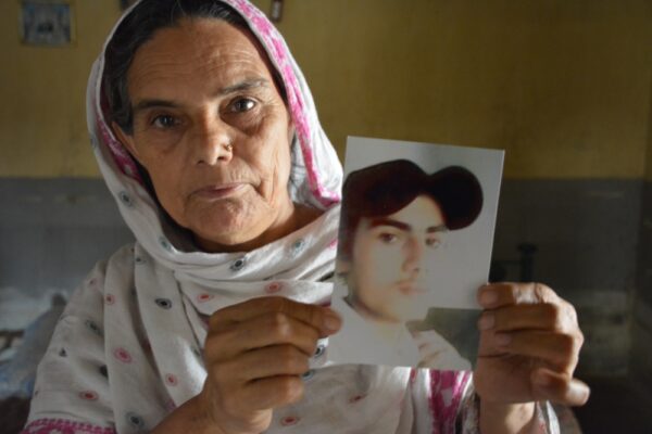 Eine ältere Frau mit Kopftuch hält ein Foto hoch. Darauf zu sehen ist ein junger Mann mit Baseball-Mütze.