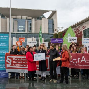 Lieferkettengesetz: Globaler Druck auf den Bundeskanzler 5 Eine Gruppe Menschen steht vor einem modernen Gebäude und hält Transparente und Plakate.