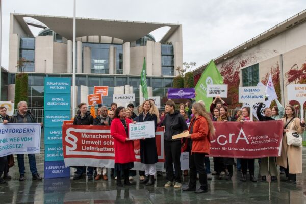 Lieferkettengesetz: Globaler Druck auf den Bundeskanzler 3 Eine Gruppe Menschen steht vor einem modernen Gebäude und hält Transparente und Plakate.
